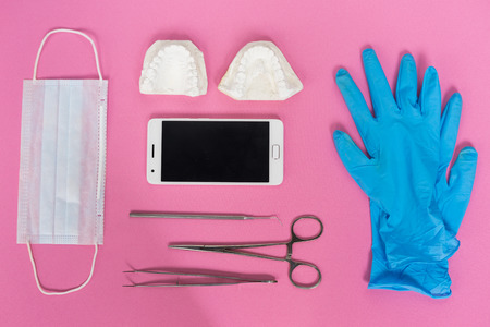 on a pink surface are blue gloves, a smartphone, dental instruments and a white plaster cast of teethの写真素材