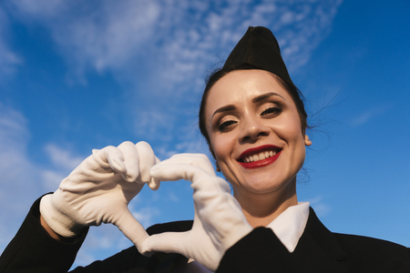 happy young woman stewardess in uniform smiling under blue skyの写真素材
