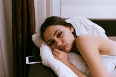 sleepy young girl lies in bed, under a white blanket, does not want to get up
