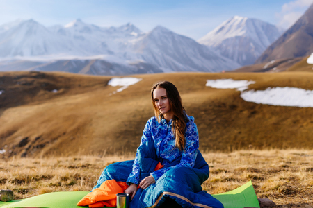 young active girl sitting in a blue sleeping bag on a background of the Caucasian mountainsの写真素材