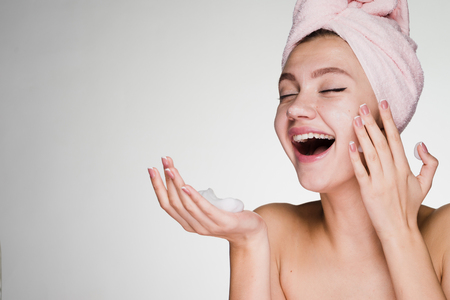 happy laughing girl with towel on head applying face cleansing foamの写真素材