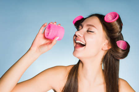 a laughing young girl makes a fashionable hairstyle with a large pink curlerの写真素材