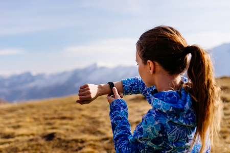 cute young girl in a blue jacket travels through the Caucasus mountains, watches time on a wristwatchの写真素材