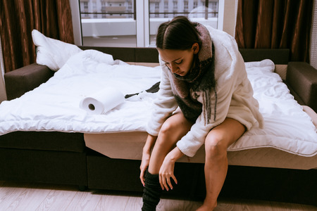 woman is sitting on the bed and putting on a stockingの写真素材
