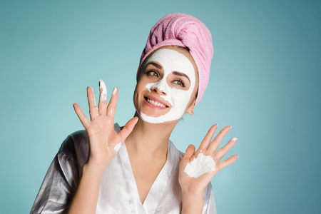 happy sweet girl with a pink towel on her head puts a white nutritious mask on her faceの写真素材
