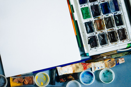 on a blue background there are paints and a white sheet of paperの写真素材