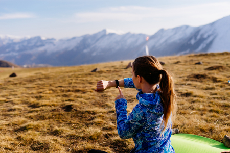 woman tourist looking at fitness bracelet on the background of mountains on a sunny dayの写真素材