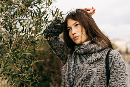 stylish young girl in glasses and with long hair walking and posing outdoorsの写真素材