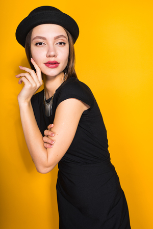 attractive young girl in black dress and hat posing, demonstrating expensive jewelryの写真素材