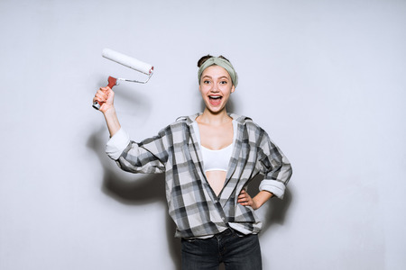 happy young girl in a plaid shirt doing repairs in a new apartment, holding a roller for painting the wallsの写真素材