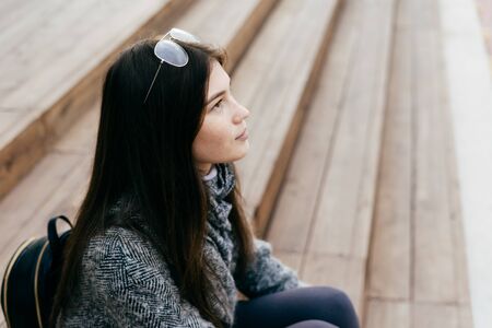 nice dark-haired girl sitting on the steps, in a gray coat, street style