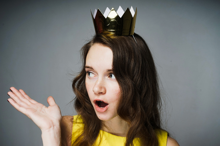 lovely surprised girl with a golden crown on her head asks a questionの写真素材
