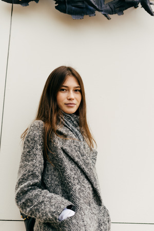 cute young dark-haired girl in gray coat walking around the city posingの写真素材