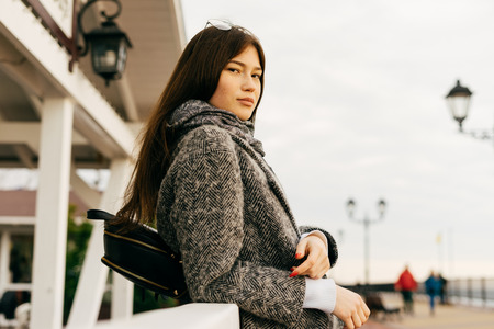 beautiful dark-haired girl in a stylish gray coat walking around the city and posingの写真素材