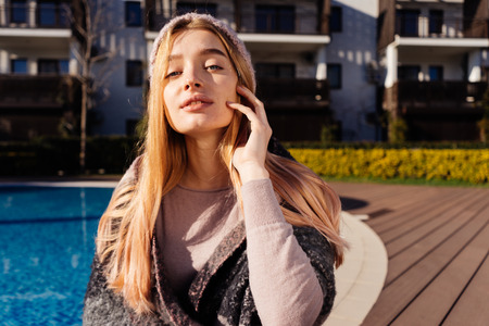 beautiful attractive girl with light code and blond hair posing by the pool in the sun, wearing a...