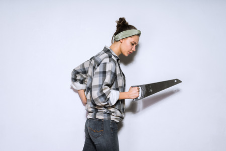 a young girl in a plaid shirt is holding a sharp saw, will do repairsの写真素材