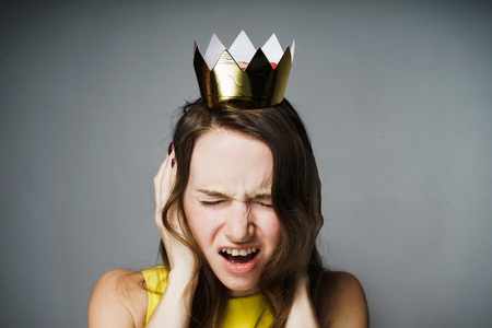 Discontented young girl covered her ears, her head was crowned with a golden crownの写真素材