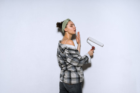 young girl in old shirt colors the wall with a platen roller in white, doing repairsの写真素材