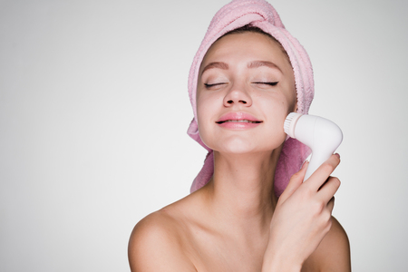 happy beautiful young girl with a towel on her head doing face cleansing with a special electric brushの写真素材