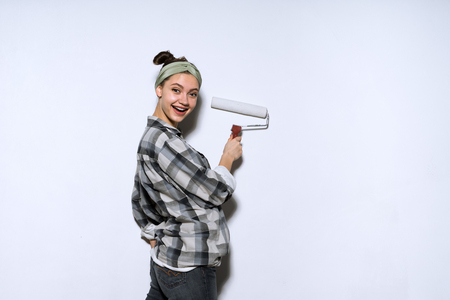 happy young girl painter in plaid shirt color paint roller in white, repairの写真素材