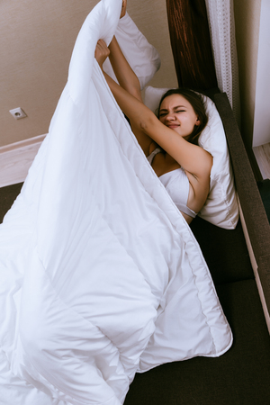 sleepy sweet young girl wakes up early, lies in bed under a white blanketの写真素材