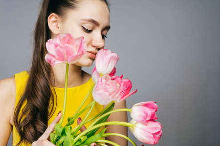 woman on a gray background holds a bouquet of pink flowers in her handsの写真素材