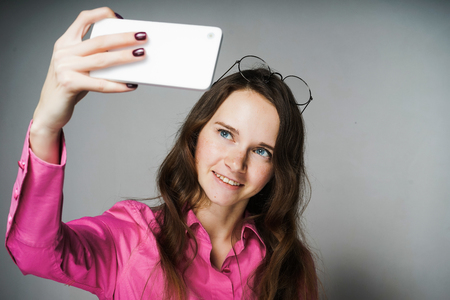 beautiful blue-eyed young woman in a pink shirt smiles and makes selfieの写真素材