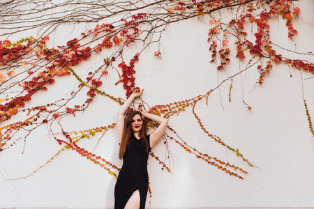 luxurious attractive long-haired girl in a black dress posing against a white wall, enjoying a rich life and relaxingの写真素材