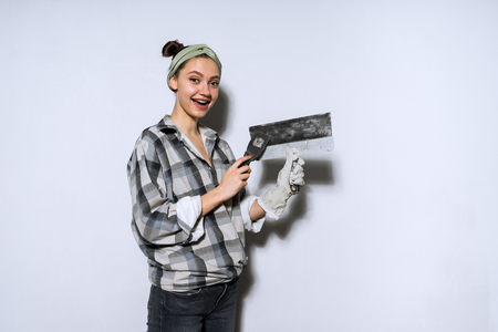 happy young girl in a plaid shirt holding a spatula, doing repairs in her new apartmentの写真素材