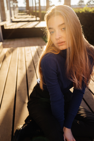 beautiful blue-eyed young blonde woman in blue sweater posing outdoors in the sunの写真素材