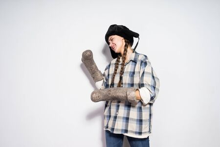 funny young girl in a fur hat waits in the winter, holds gray felt bootsの写真素材