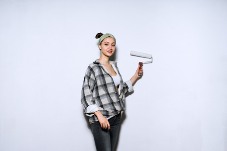 beautiful young woman in a plaid shirt doing repairs, paints a wall with a rollerの写真素材
