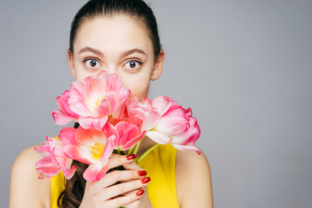 cute young girl surprised, holding a bouquet of fragrant pink flowersの写真素材