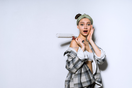 surprised young girl doing repairs in a new apartment, holding a roller for painting wallsの写真素材