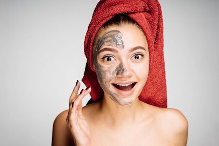 happy young girl with a red towel on her head applies a useful clay mask on the faceの写真素材