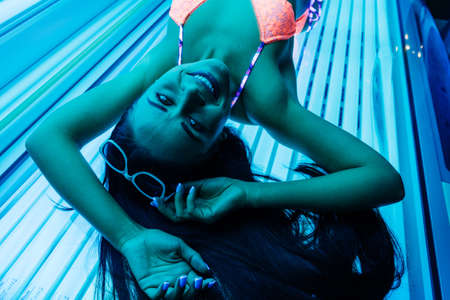 happy slender girl sunbathing in a horizontal tanning bed under ultraviolet rays, smilingの写真素材