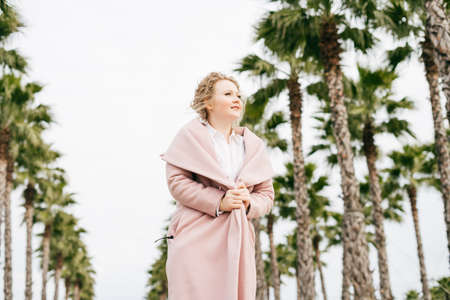 stylish young woman in a pink trendy coat walking through a spring park and smilingの写真素材