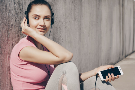 beautiful sports girl listening to music on headphones, resting after a hard workout outdoorsの写真素材