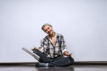smiling young girl sitting on the floor in her new apartment, holding a spatula, repairingの写真素材