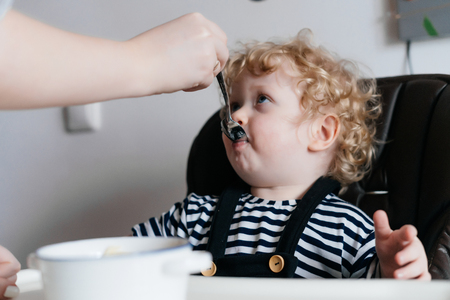 caring mother feeds her young son with useful porridge, family breakfastの写真素材