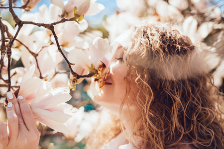 beautiful smiling girl sniffs fragrant magnolia flowers, walks in the park on a warm spring dayの写真素材