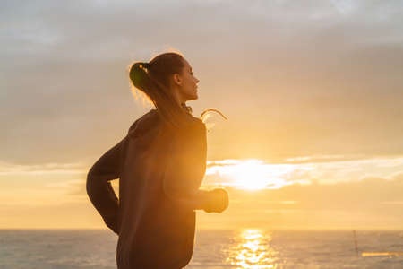 zealous young girl runs along the quay at sunset, leads a healthy lifestyle, a lot of energyの写真素材