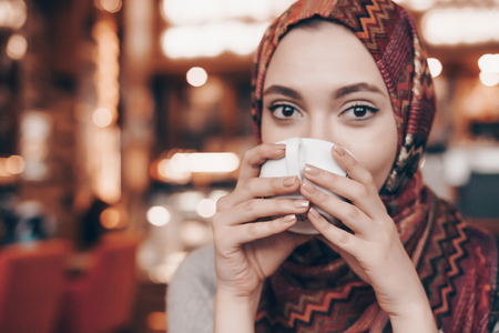 nice beautiful Arab girl with a handkerchief n agolovo drinks fragrant coffee in a cafeの写真素材