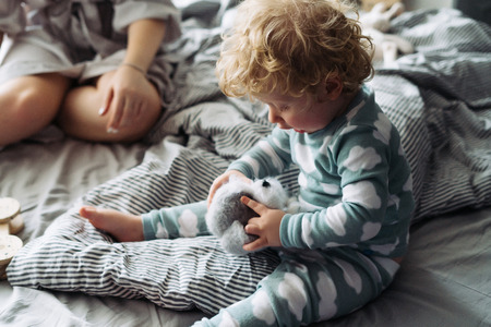 little curly toddler baby boy sitting on the bed and holding his favorite toy