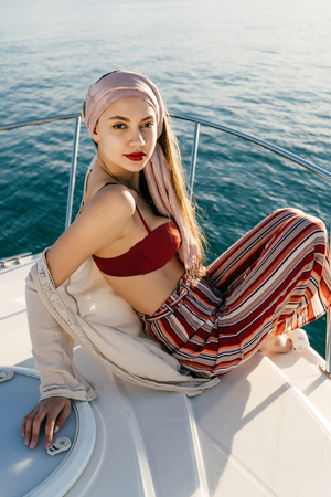 an attractive confident girl in stylish clothes sits on her white yacht, enjoys a rich life and restの写真素材