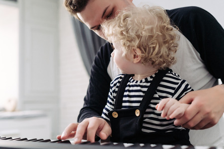a friendly family, a young dad teaches to play his little curly son on the piano, spend time togetherの写真素材