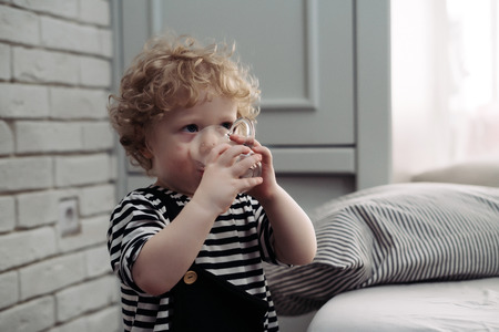 cute curly toddler boy drinking water from mugの写真素材