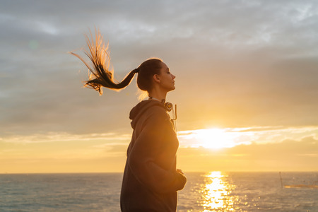 a sporty young girl trains in front of a marathon, runs by the sea in the rays of the evening sun