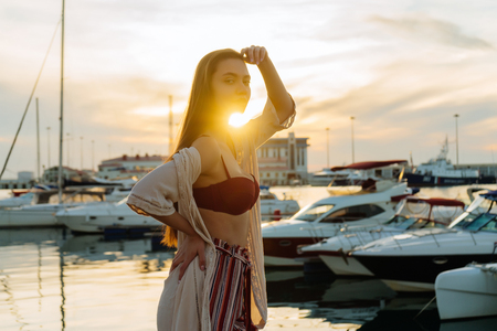 luxurious long-haired girl in stylish summer clothes posing in the seaport in the rays of the evening sunの写真素材