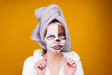 cute young girl with a towel on her head after a shower smiles, on her face a mask with a muzzle of a dogの写真素材